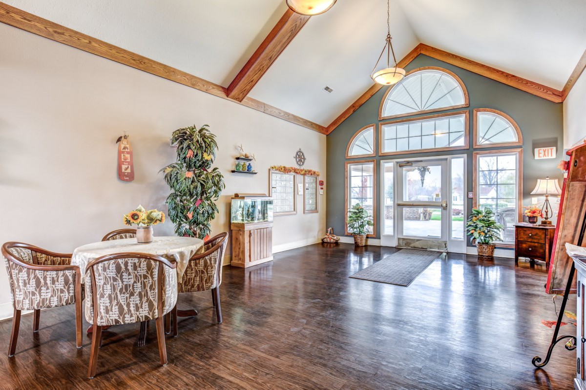 A bright and welcoming lobby area with high ceilings, wood flooring, comfortable seating, and natural light streaming through large windows.