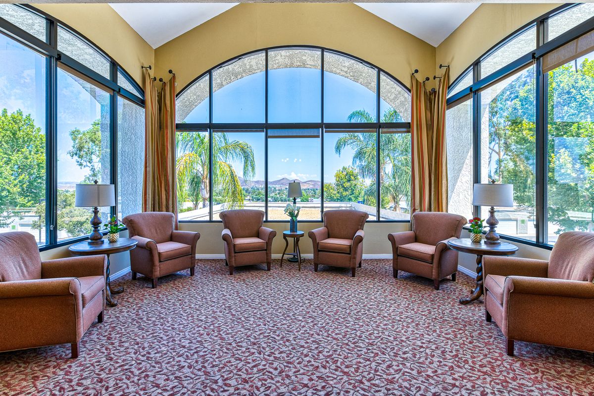 A spacious lounge area with comfortable chairs and large windows overlooking palm trees.