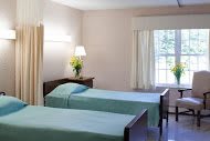 A minimalist bedroom with two twin beds, a lamp, and a window adorned with curtains.