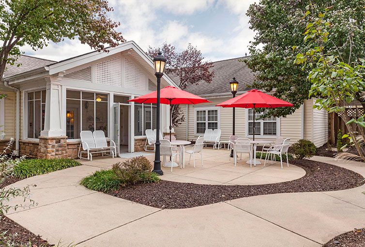 A charming outdoor patio area with red umbrellas and white furniture, surrounded by a well-maintained garden.