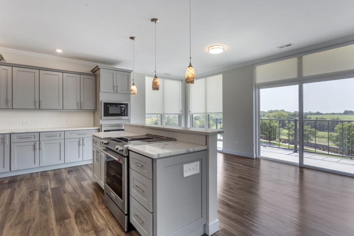 A modern kitchen with an island and pendant lights, featuring wood flooring and open space design.