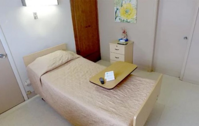 A tidy, minimalist bedroom with a single bed, small cabinet, and warm lighting.