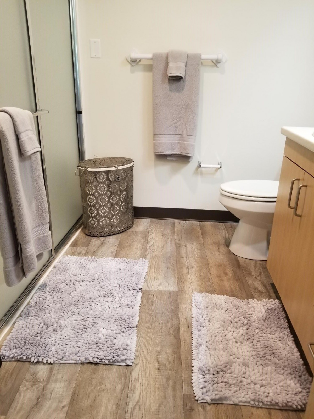 A modern bathroom featuring neatly arranged towels, rugs, and a laundry hamper.