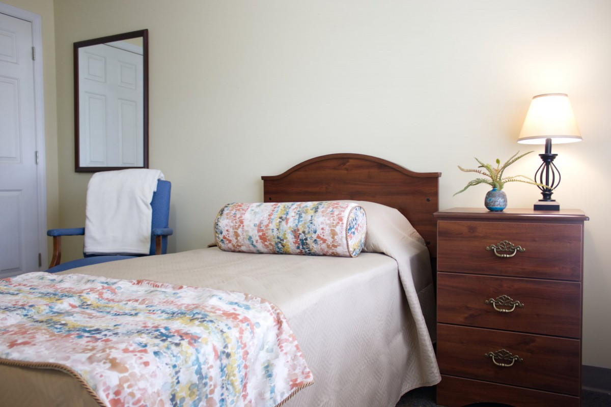 A cozy bedroom with a twin bed, floral pillow, and wooden nightstand.