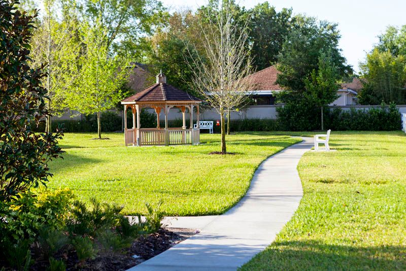 A serene park scene featuring a winding pathway leading to a wooden gazebo, surrounded by lush green grass and trees.