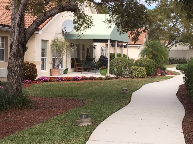 A quaint house with a green awning, surrounded by well-maintained landscaping and a curved pathway.