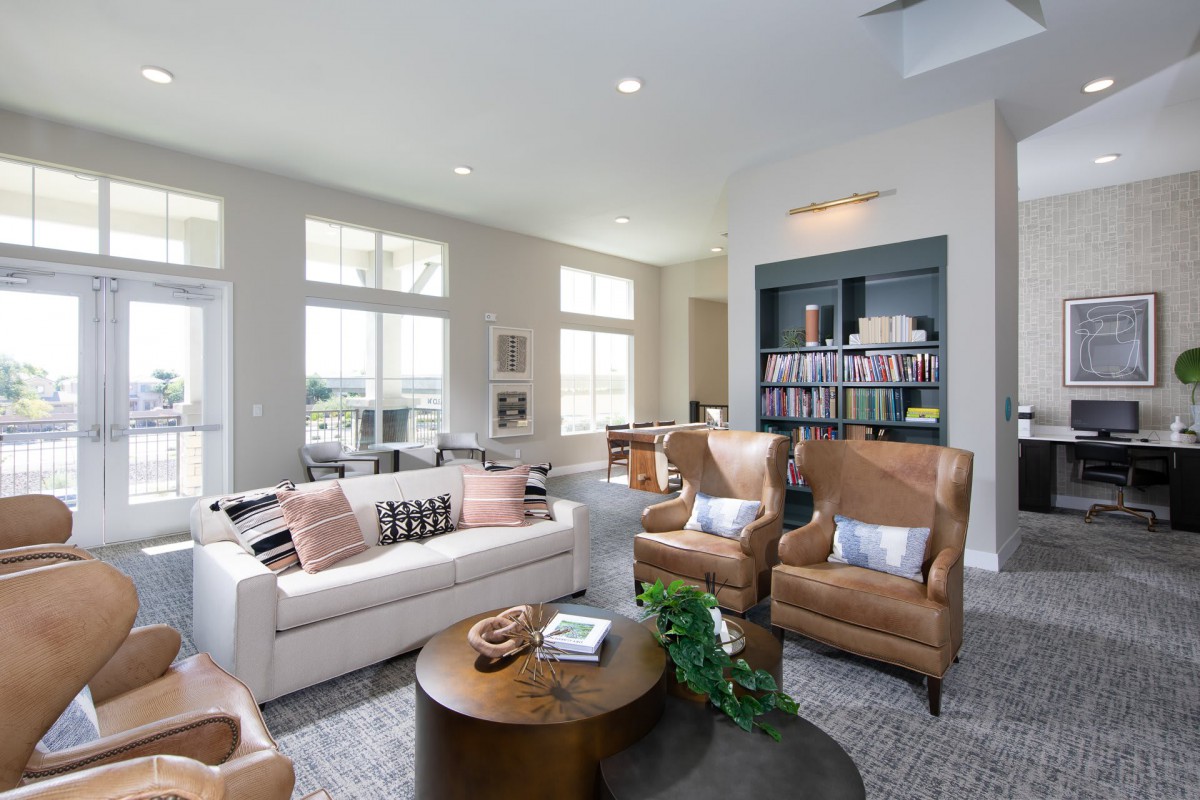 A modern and cozy living room featuring a plush sofa, comfortable leather chairs, a round wooden coffee table, and a well-stocked bookshelf.