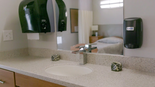 A modern bathroom sink with a sleek faucet, reflecting light and leading into a cozy bedroom.