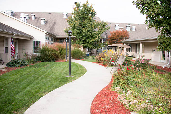 A beautifully landscaped garden with a winding pathway, benches, and a swing surrounded by lush greenery and trees.