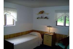 A simple bedroom with a single bed and a nightstand under two small windows.