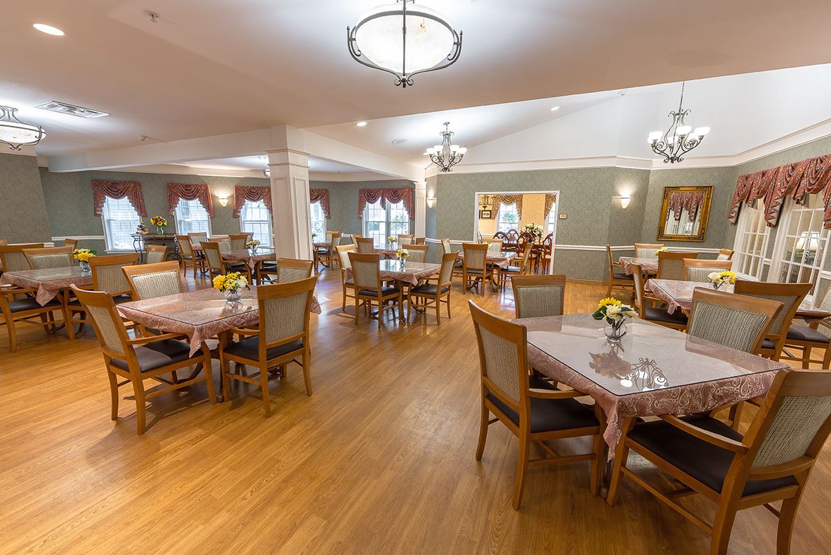 A spacious dining room with multiple tables and chairs, adorned with chandeliers and a wooden floor.