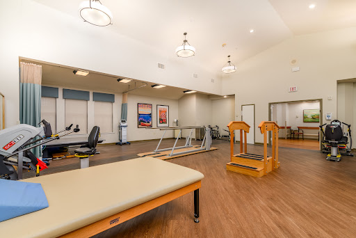 An interior view of a physical therapy facility, featuring exercise equipment and a therapy table.