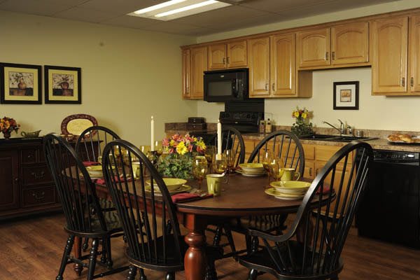 A cozy dining area with a wooden table set for a meal, featuring candles and a flower centerpiece in a warm kitchen setting.