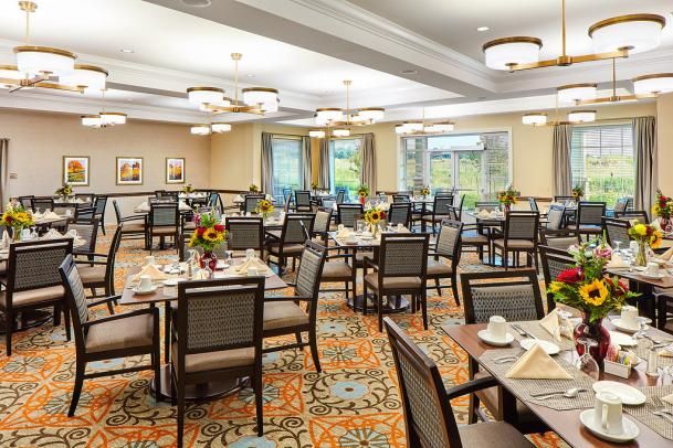 An elegantly set dining room with multiple tables and chairs, featuring warm lighting and large windows.