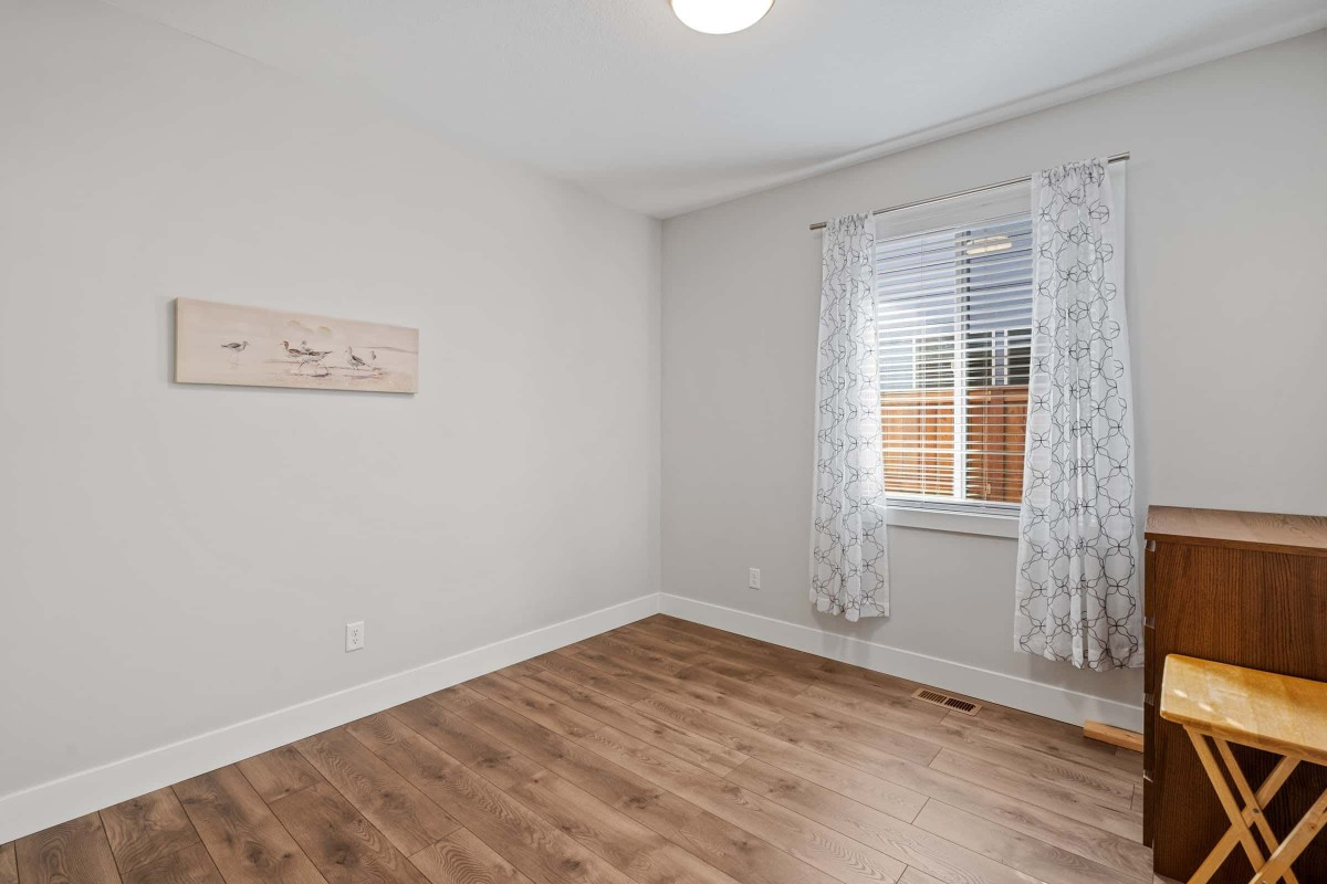 A minimalist empty room with wood flooring and a window adorned with patterned curtains.