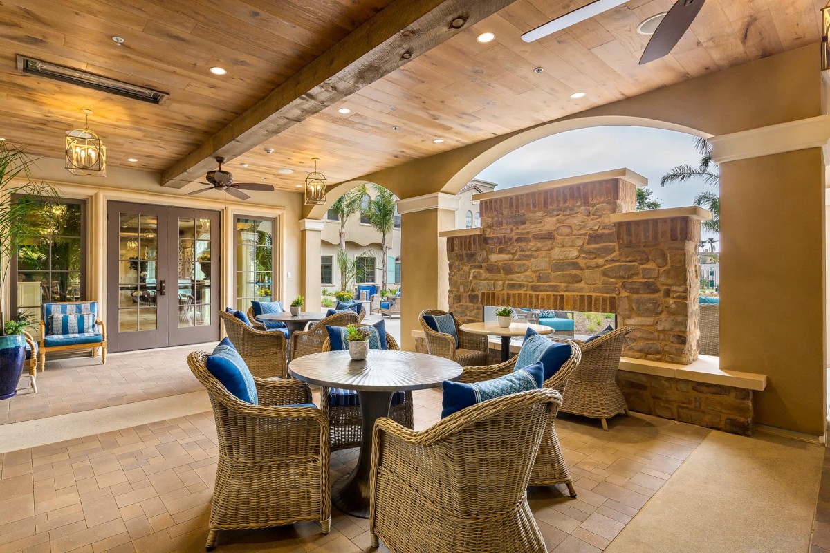 A cozy outdoor patio with wicker furniture and blue cushions, featuring tables and chairs under ceiling fans.