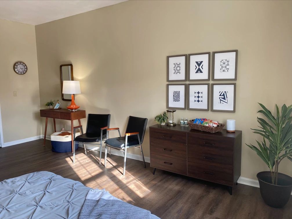 A stylish bedroom with a dresser, chairs, and framed artwork.