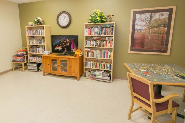 A cozy living room with bookshelves, a television, and a clock on the wall.