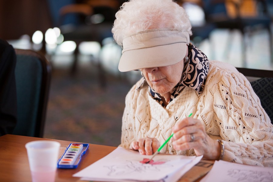 An elderly woman engaged in painting with watercolors.