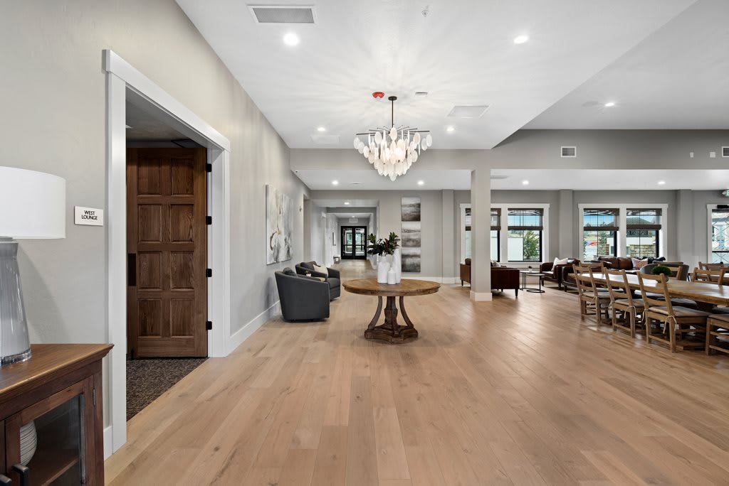 A spacious and modern interior with hardwood floors, featuring a chandelier, table, and chairs in a well-lit living area.