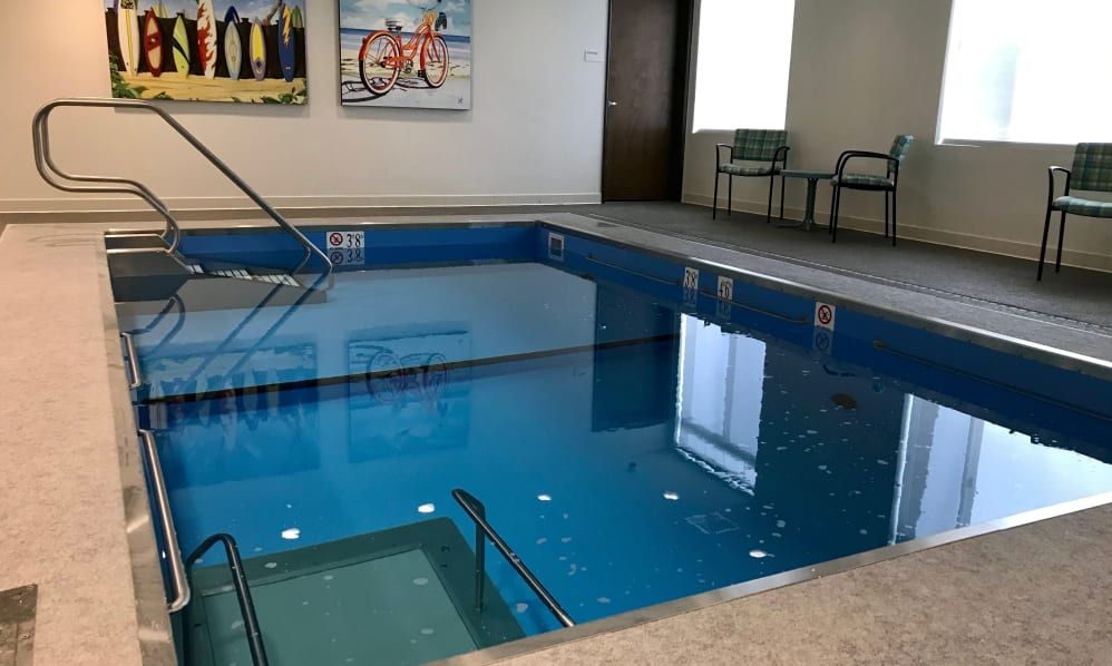 An indoor therapy pool with exercise equipment and chairs by the side.