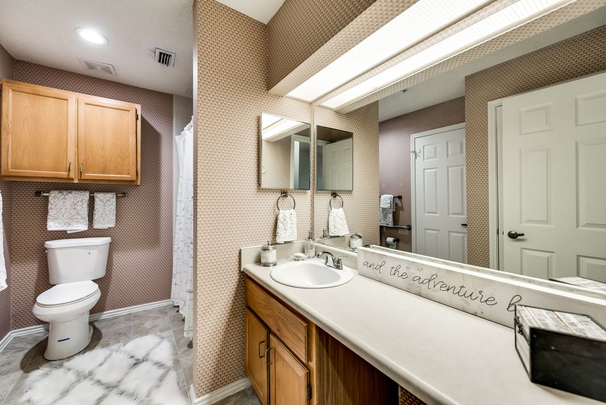 A well-lit bathroom with a large mirror, sink, and wooden cabinets.