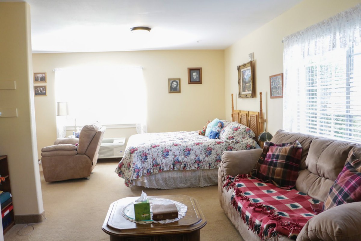 A cozy bedroom with a bed, sofa, and recliner, decorated with framed pictures and blankets.