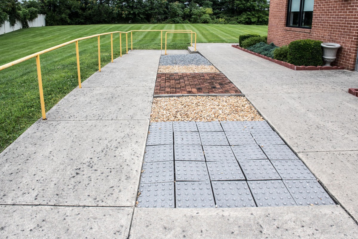 An outdoor walkway featuring various textured sections, including concrete, pavers, and stones.