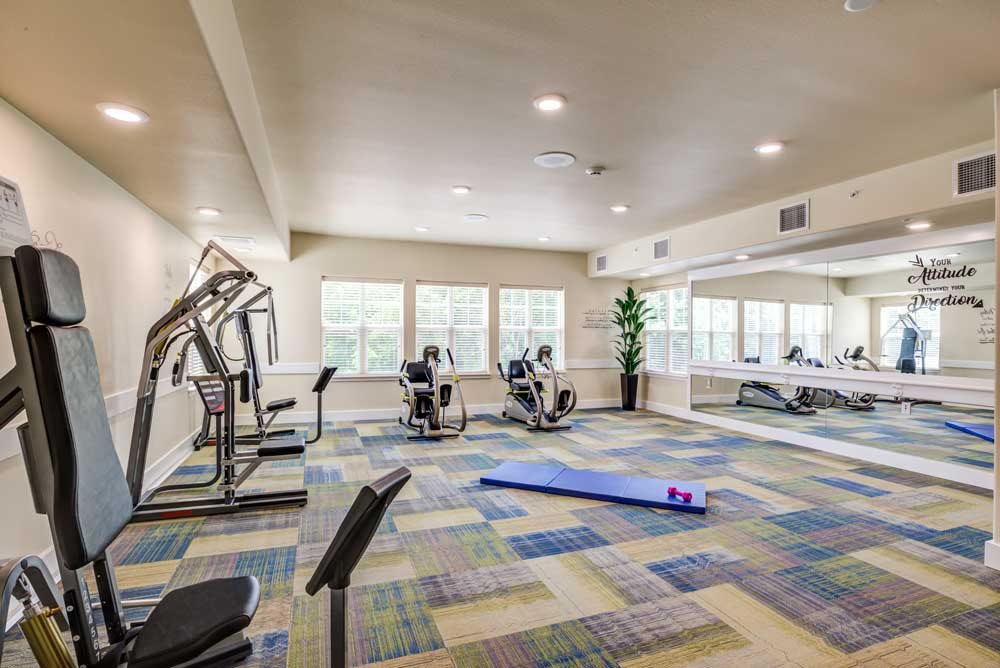 A well-equipped gym with exercise machines, a yoga mat, and dumbbells in a brightly lit workout space.