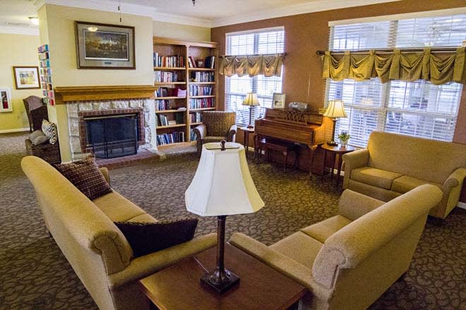 A cozy living room with sofas, a fireplace, bookshelves, and a piano.