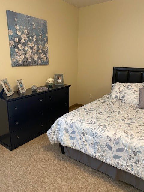 A cozy bedroom with a floral-themed bedspread and wall art, complemented by a dresser with framed photos.