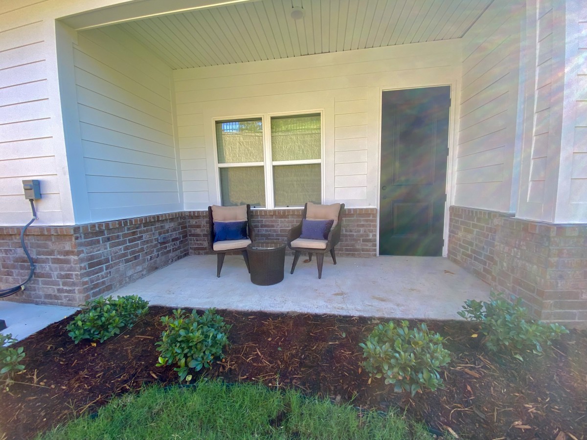 A cozy porch with two chairs and a table surrounded by landscaped plants.