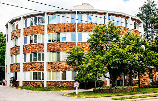 A modern round building with brick facade and large windows, surrounded by greenery.
