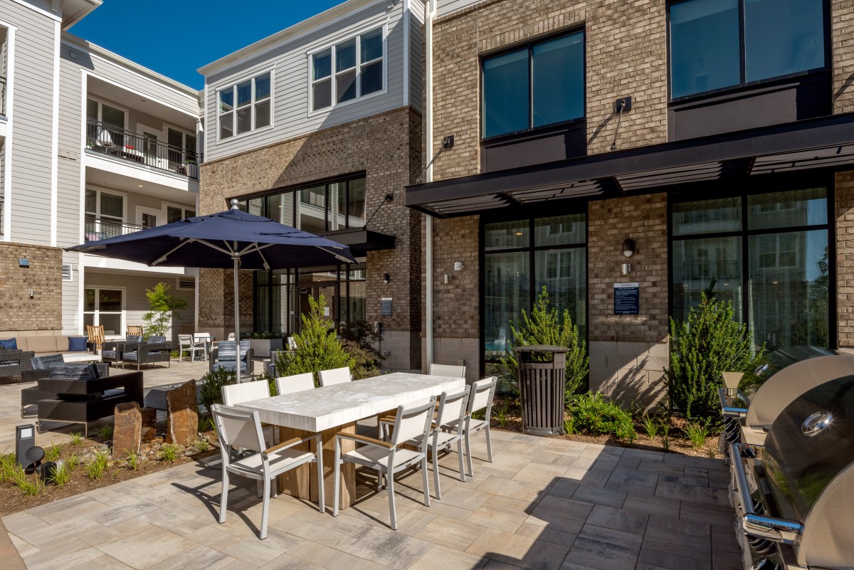 A modern outdoor patio featuring a dining set with an umbrella, surrounded by greenery.