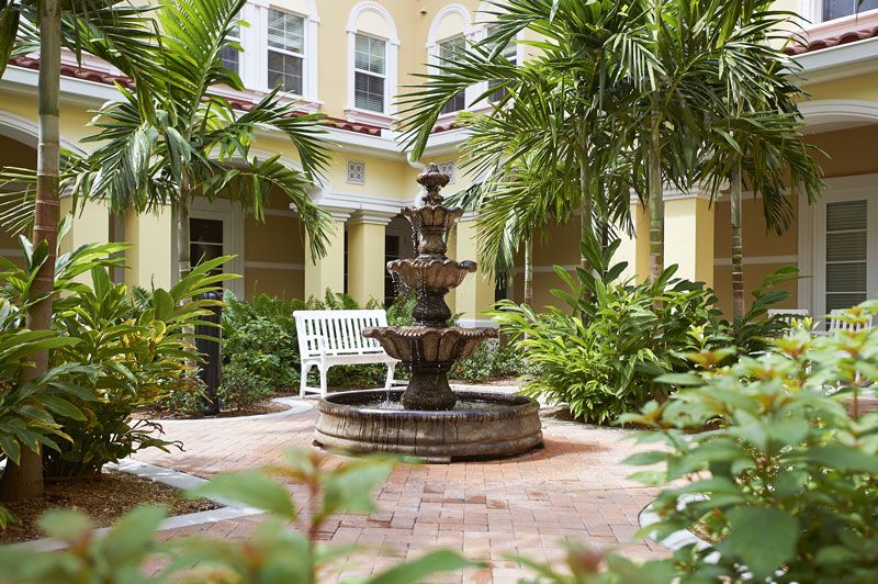 A tranquil courtyard with a central fountain surrounded by tropical plants and palm trees.