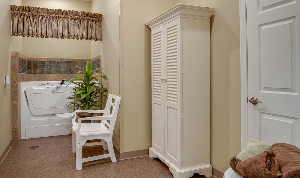 A bathroom with a white wardrobe, plastic chair, and a potted plant.