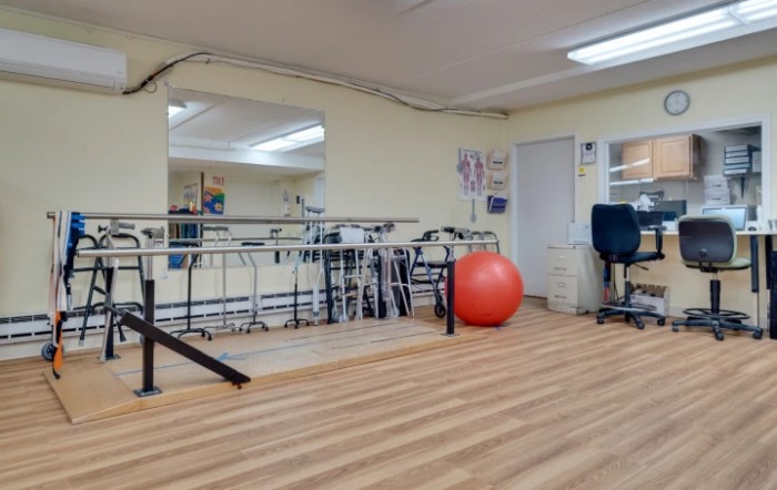 A physical therapy room equipped with parallel bars and a red exercise ball.