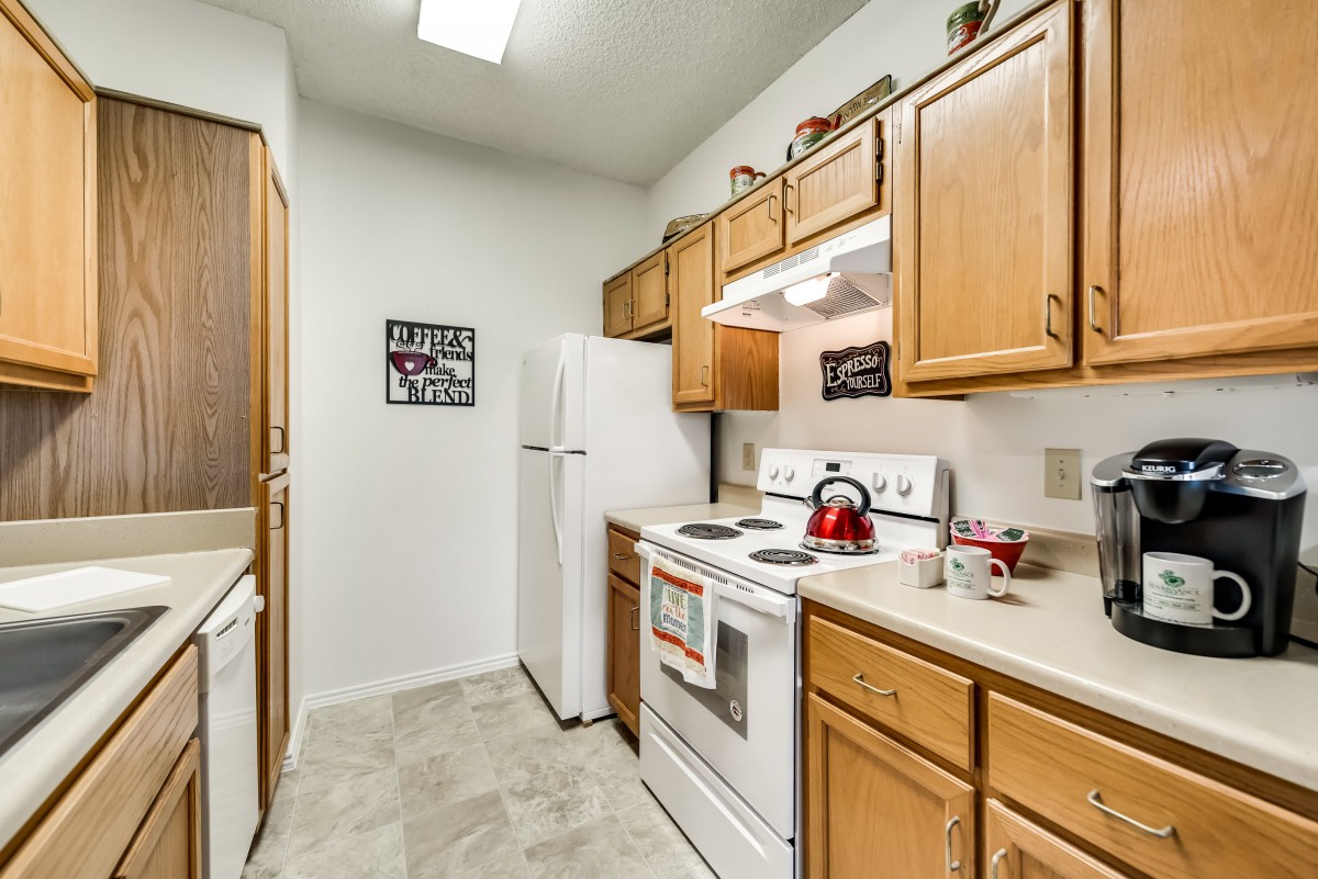A cozy apartment kitchen with wooden cabinets, a white stove, and refrigerator.