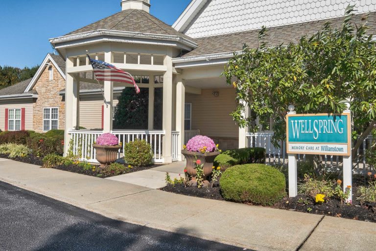 A welcoming building entrance with a flag, well-maintained landscaping, and a sign.