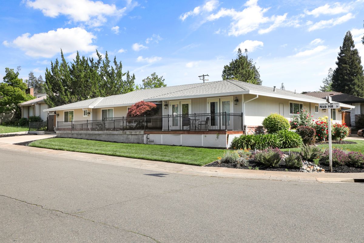 A suburban house with a well-maintained lawn and trees under a clear blue sky.