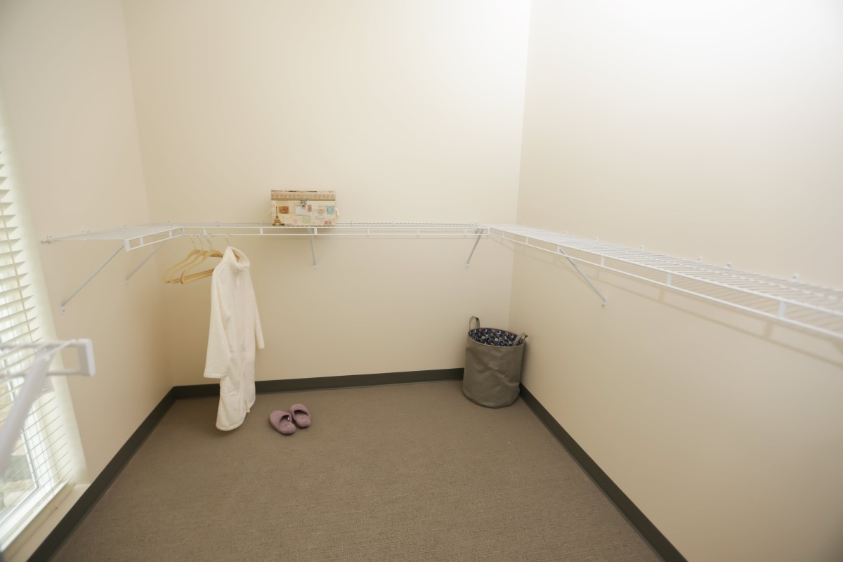 An empty changing room with a bathrobe, sandals, and a trash can.