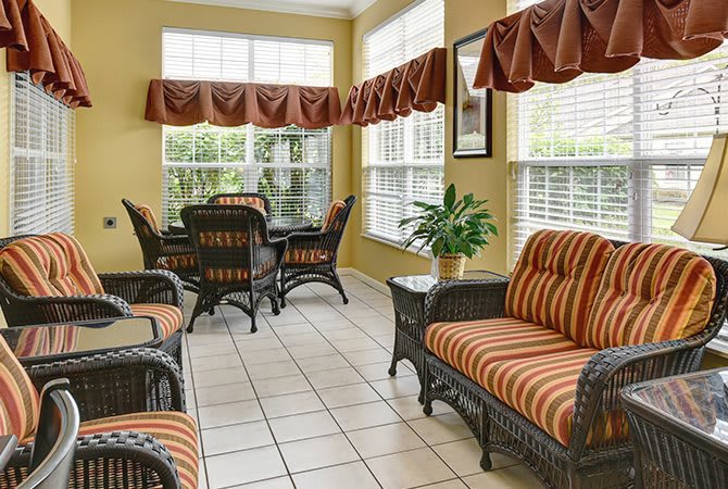 A sunroom with wicker furniture featuring striped cushions, tile flooring, and large windows adorned with curtains.