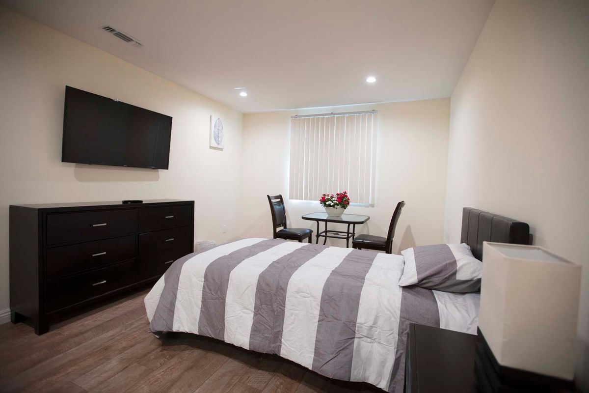 A modern bedroom with a striped bedding set, a wall-mounted television, and a small dining area.