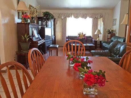 A cozy living and dining area with a wooden table, floral arrangements, and a piano.