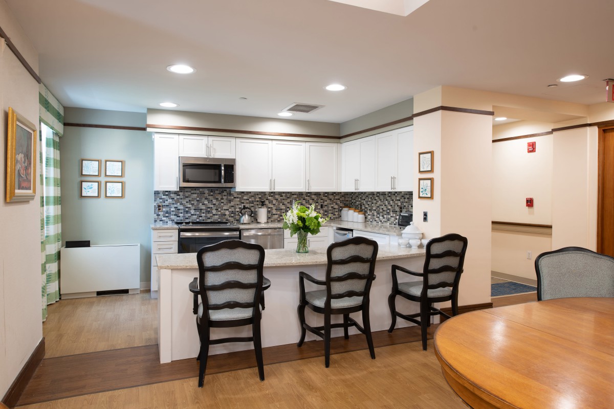 A modern kitchen with a sleek design featuring a white countertop, stylish bar stools, and stainless steel appliances.