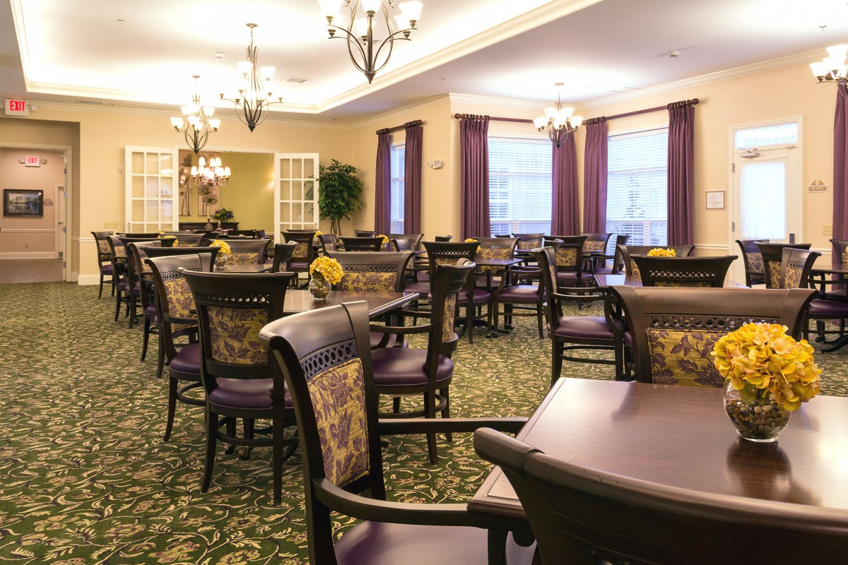 A spacious dining room with elegant dcor, featuring multiple tables and chairs, chandeliers, and a patterned carpet.