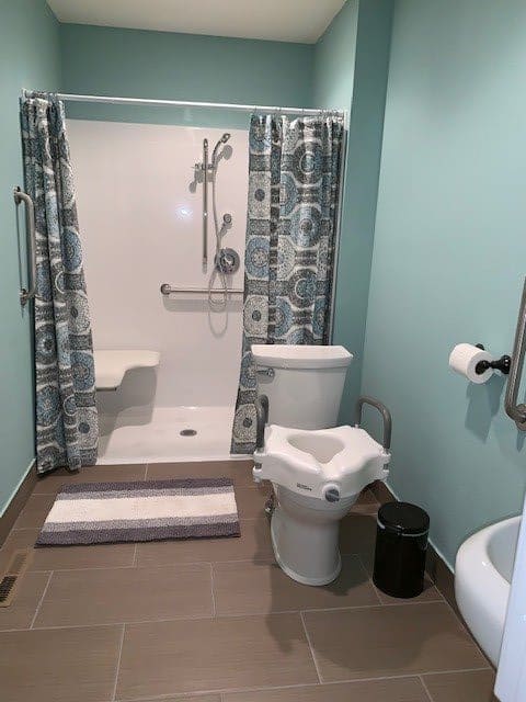 A modern, handicap-accessible bathroom featuring a shower with grab bars and a toilet with additional support.