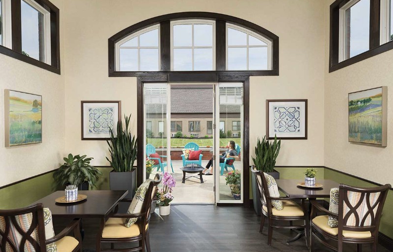 A cozy interior space with a view of the patio, featuring comfortable seating, indoor plants, and framed artwork on the walls.