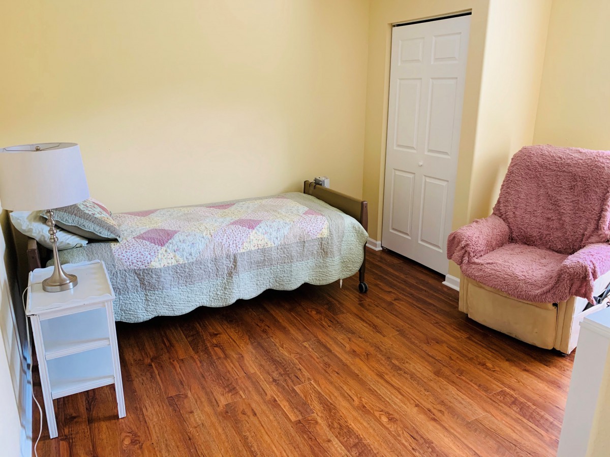 A simple bedroom featuring a single bed, hardwood flooring, and a cozy chair.