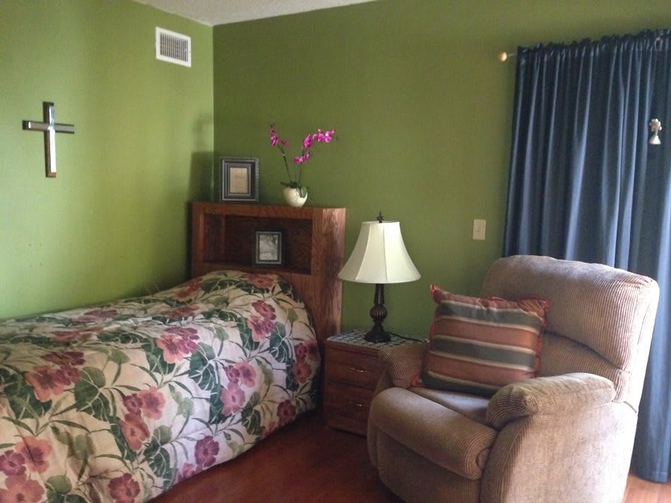 A cozy bedroom with green walls, featuring a floral bedspread, wooden furniture, and a comfortable armchair.